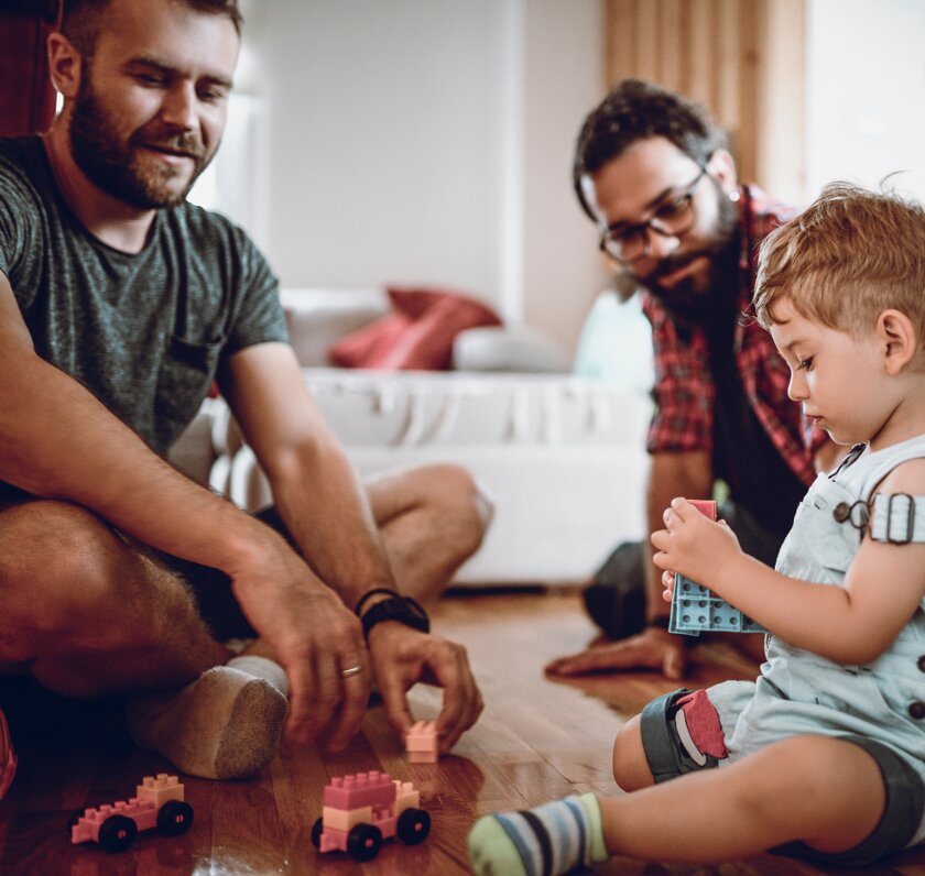 Two men and and child playing with toys on the floor